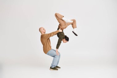 Gri arka planda stüdyoda akrobatik denge uygulayan günlük kıyafetli bir çift.
