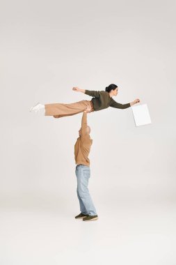 Günlük kıyafetli erkek akrobat. Alışveriş çantalı kadını kaldırıyor. Stüdyoda neşeli bir duruş sergiliyor.