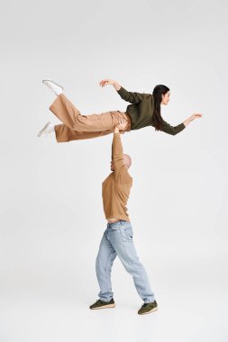 artistic acrobat duo with man lifting and supporting young woman in studio on grey backdrop clipart