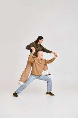 Artistik bir çiftin akrobatik performansı, günlük giysiler giymiş bir kadın, gri üzerinde erkeğin kucağında denge kuruyor.
