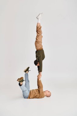 Artistik bir çiftin akrobatik performansı, günlük giysiler giymiş bir kadın, gri üzerine erkeğin ellerinde denge kuruyor.