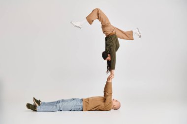 Artistik bir çiftin akrobatik performansı, günlük giysiler giymiş bir kadın, gri üzerine erkeğin ellerinde denge kuruyor.