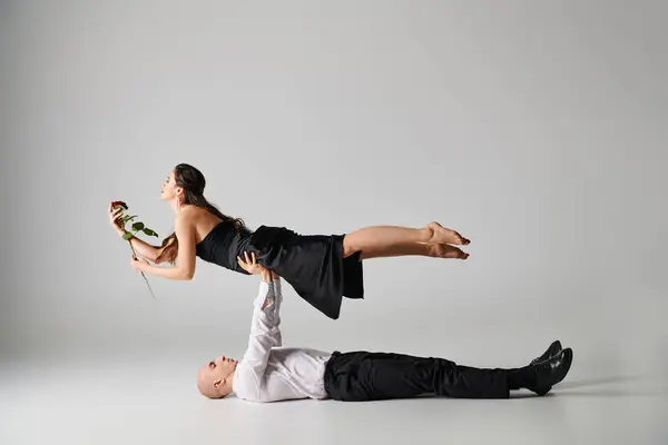男性ダンサーが床に横たわり パフォーマンス中にバラとドレスで女性の体を持ち上げる — ストック写真