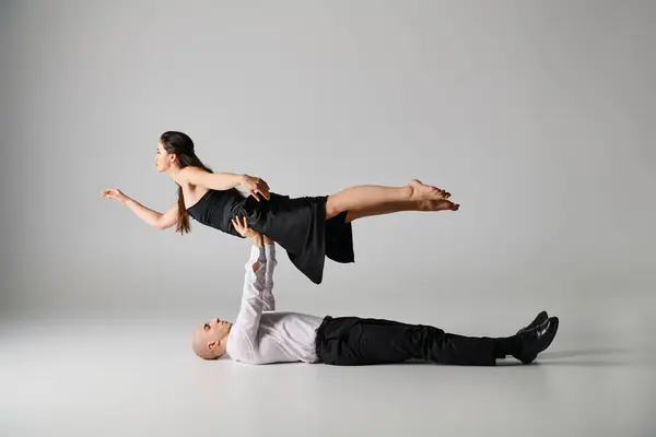 男は床に横たわり 灰色の背景でダンスパフォーマンス中にドレスで女性の体を持ち上げる — ストック写真