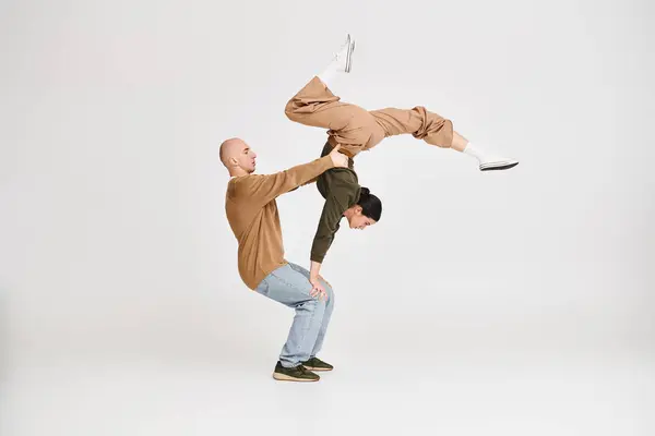 stock image Couple in casual attire performing an intricate acrobatic balance in studio on grey background