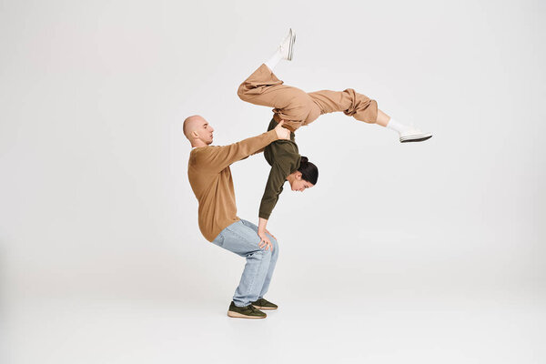 Couple in casual attire performing an intricate acrobatic balance in studio on grey background