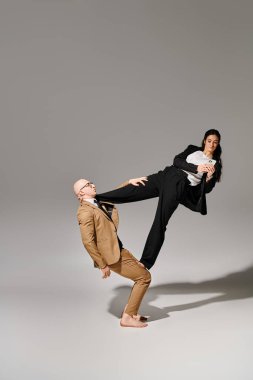 young businesswoman using smartphone and balancing with help of acrobat man in suit in studio clipart