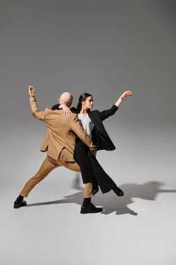 Takım elbiseli iş çifti gri arka plan ve akrobatlarla stüdyoda dinamik bir dans gösterisi yapıyor.