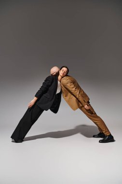 Young artistic couple in business attire performing a mirror dance move in studio with grey backdrop clipart