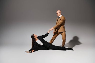 female acrobat in elegant corporate suits executing a split and holding hands with man in studio clipart