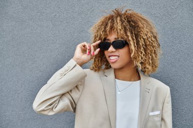 Ofis binasının yakınında güneş gözlüğü takan, tel ve kıvırcık saçlı mutlu Afro-Amerikan kadını.