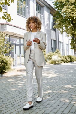 Diş teli takmış mutlu Afro-Amerikan girişimci ofis binasının yakınında akıllı telefonuyla yürüyor.