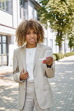 Diş teli takmış mutlu Afro-Amerikan girişimci ofis binasının yanındaki akıllı telefonunu kullanıyor.