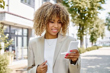 Diş teli takmış Afro-Amerikan iş kadını ofis binasının yakınında akıllı telefonuyla yürüyor.