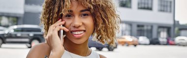 banner of happy radiant curly-haired black woman having phone call in urban setting, smartphone clipart