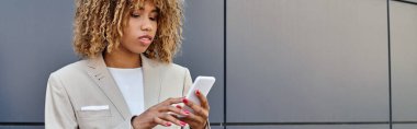 Kıvırcık saçlı, takım elbiseli ve akıllı telefon, afiş kullanan Afro-Amerikan iş kadını.
