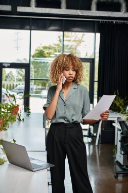 Çoklu görev yapan Afrikalı Amerikalı iş kadını modern ofiste dizüstü bilgisayarın yanında nöbet tutuyor.