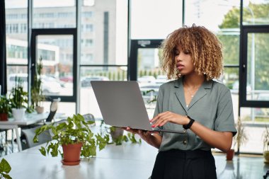 İyi ışıklandırılmış bir ofiste dizüstü bilgisayar kullanan Afro-Amerikalı genç bir iş kadını.