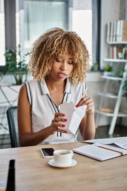 Kıvırcık Afrikalı Amerikalı kadın elinde erişteyle masada yemek çubuğu tutuyor.