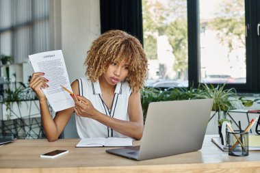 Odaklanmış Afrikalı Amerikalı kadın dizüstü bilgisayardaki video görüşmesi sırasında kalemle kontrat gösteriyor.