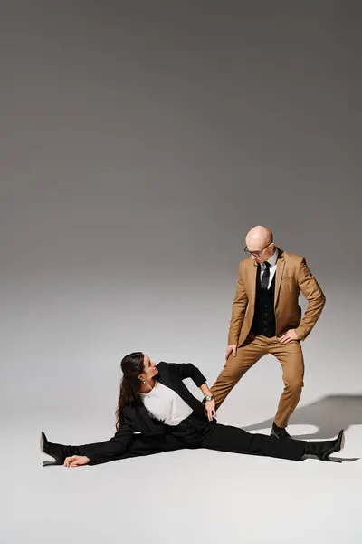 stock image female acrobat in elegant corporate suits executing a split and holding hands with man in studio