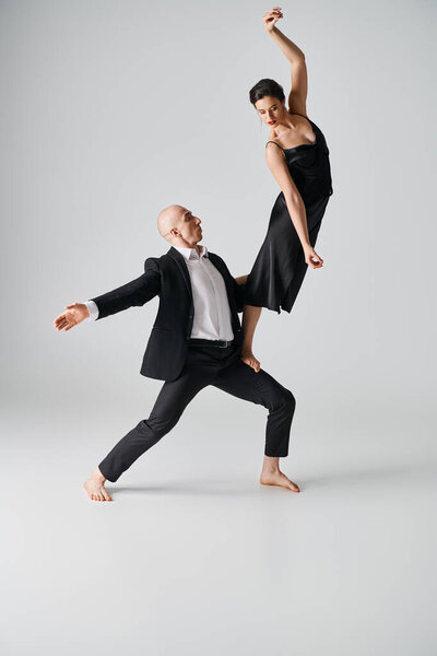 barefoot dancer in black dress balancing gracefully on leg of male partner in grey studio