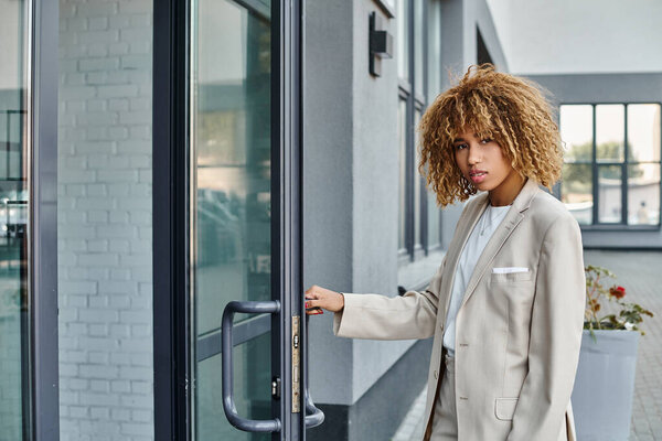 curly african american businesswoman in formal wear entering office building, young professional