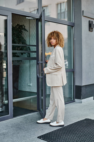 curly african american businesswoman in formal wear entering office building, young leader