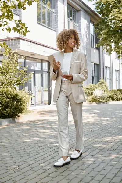 Stock image happy african american entrepreneur in braces walking with folder near office building on sunny day