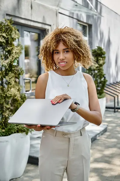 stock image happy african american woman with braces standing with her laptop near building in warm summer day