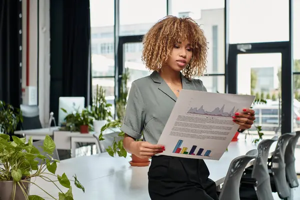 stock image Analytical african american businesswoman evaluating graphs in a dynamic office space, manager