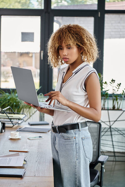 curly african american businesswoman in casual attire working on laptop in a modern office
