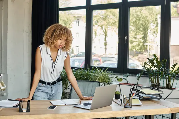 Stock image focused curly african american woman standing at her desk and looking at laptop during working day