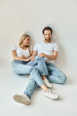 A romantic couple, the man and woman, sit close together on the ground, sharing an intimate moment of connection and love. clipart