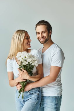Kadın nazikçe bir buket çiçeği erkeğin yanında tutuyor ve bu da çift arasında romantik ve samimi bir an yaratıyor..