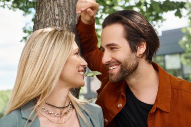 A man and a woman sharing a romantic moment, standing peacefully next to a tall tree. clipart