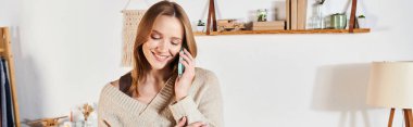 Genç ve neşeli ev hanımı modern dairede cep telefonuyla konuşuyor, yatay afiş.