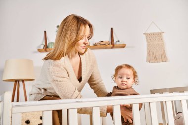 # Mutlu genç anne, küçük çocuğu destekliyor # # Bebek odasında beşikte duruyor #