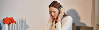 grieving woman trying to relax by listening music in headphones in dark nursery room, banner clipart
