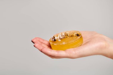 object photo of piece of natural soap with decor on it in hand of unknown woman on gray backdrop clipart