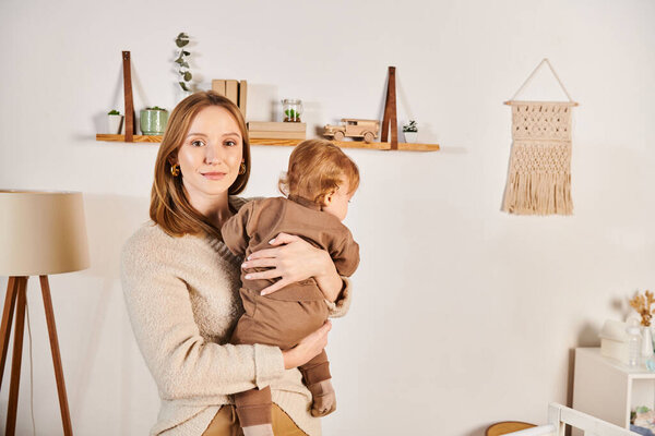 счастливая молодая женщина держит и обнимает маленького ребенка сына в детской комнате, блаженное материнство
