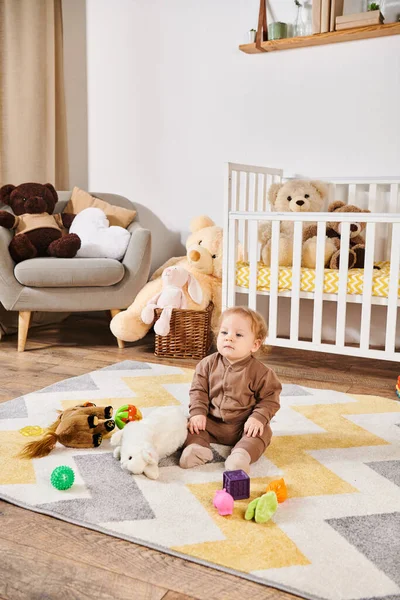 Tatlı küçük çocuk yumuşak oyuncakların yanında yerde oturuyor ve bebek odasında rahat bir beşik, mutlu bir çocukluk.