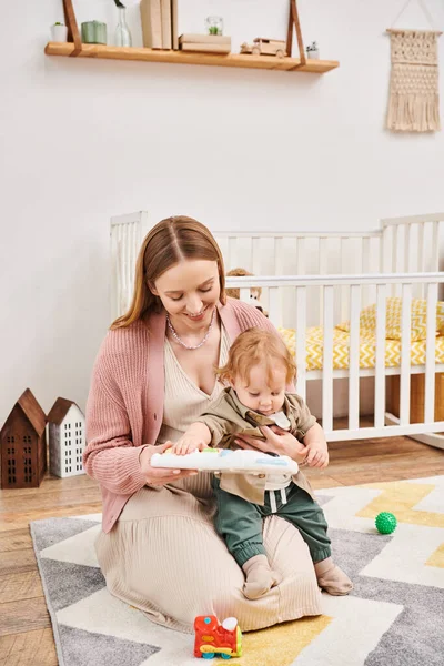 Mutlu anne, bebek beşiğinin yanında tatlı beşiği ile oynuyor. Bebek odasında, mutlu annelik.