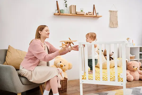 Neşeli hamile bir kadın oyuncak uçağı tutuyor. Evdeki bebek odasında küçük bir oğlu var. Annelik.