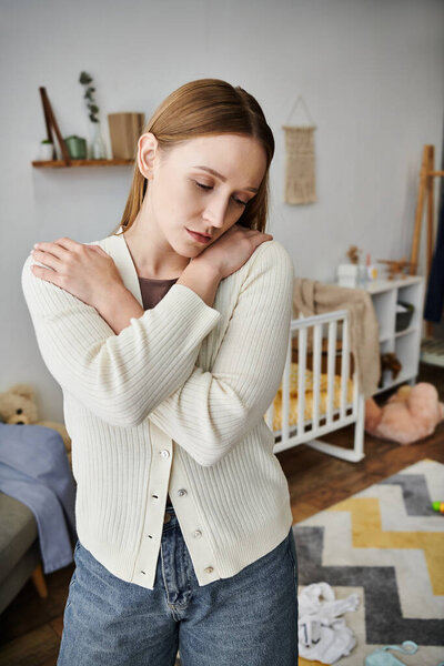 despaired young woman standing in nursery room  with baby crib and soft toys, grieving