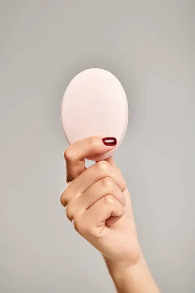 oval piece of natural soap in hand of unknown female model with nail polish on gray background