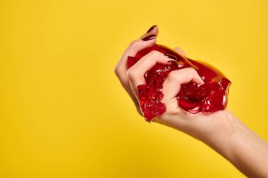 unknown female model squeezing red delicious jello in her hand on vibrant yellow background clipart