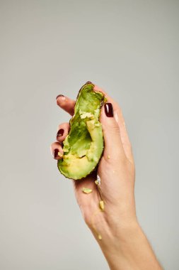 Bilinmeyen bir kadın model. Gri arka planda, elinde sağlıklı, lezzetli bir avokado tutuyor.