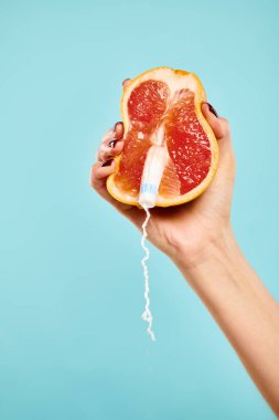 Üzerinde tampon olan lezzetli greyfurt resmi mavi arka planda bilinmeyen bir kadının elinde.