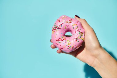 Üzerinde pembe krema olan tatlı, lezzetli bir donut. Elinde pembe arka planda tutan bilinmeyen bir kadın var.